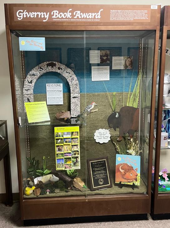 Cabinet display with an arch representing keystone species. The 2026 Giverny award-winning book is in the right foreground, and a painting of a buffalo above